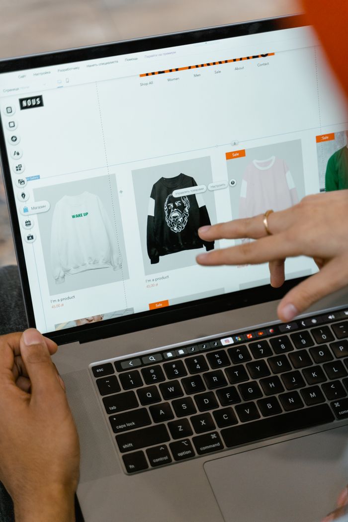 Gros plan sur des mains interagissant avec un site de shopping affiché sur l'écran d'un ordinateur portable, en intérieur.